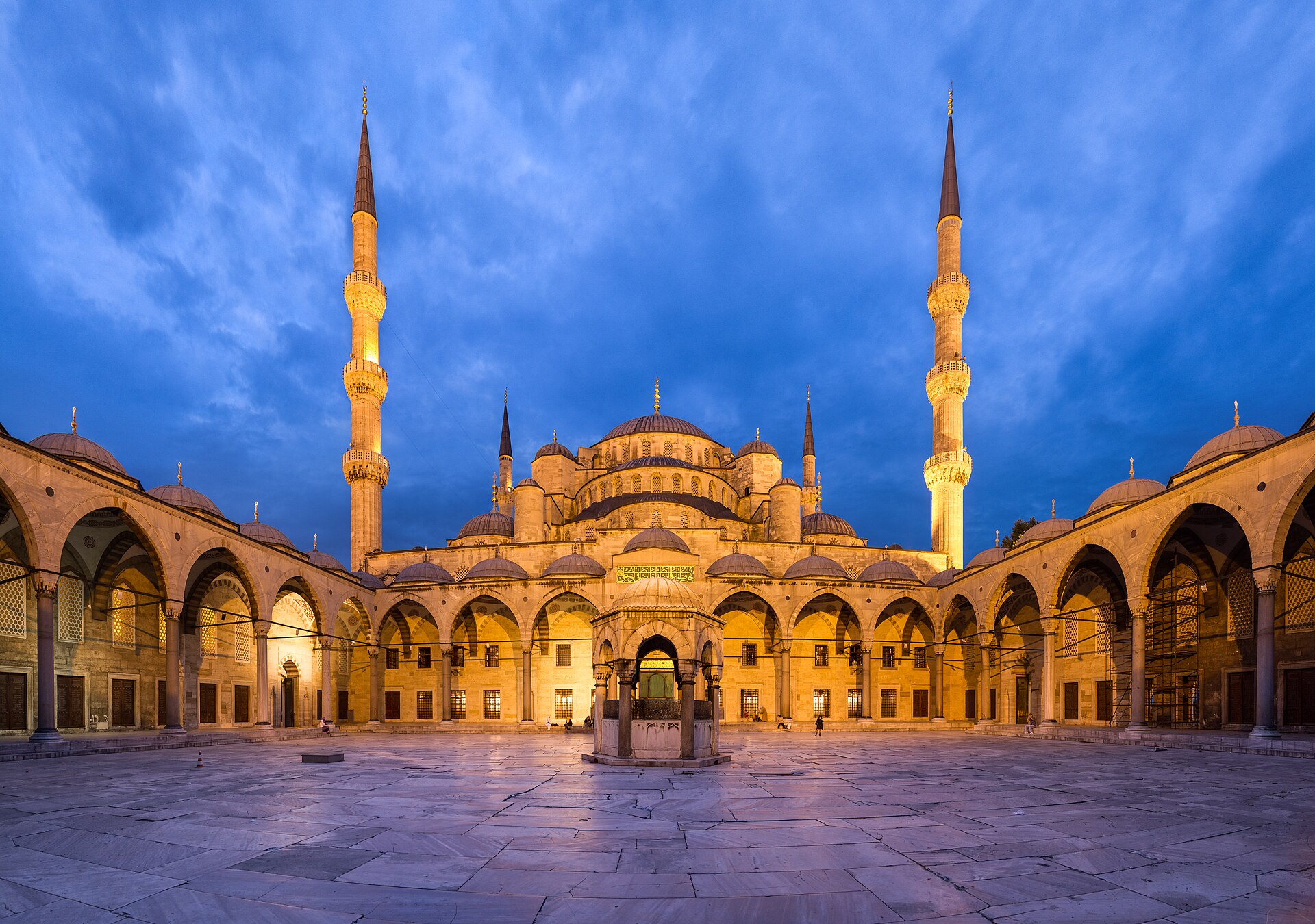 The courtyard of the Sultan Ahmed Mosque at dusk, its domes and minarets lit against a deep blue sky